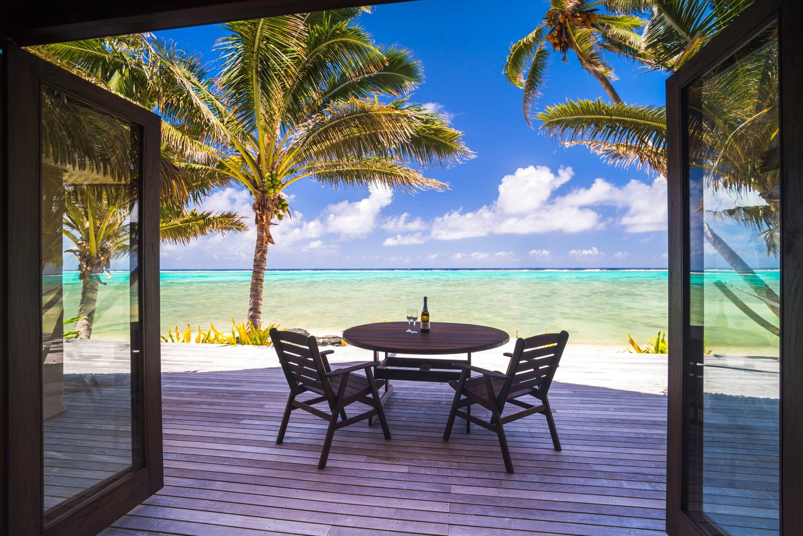 Luxury beachfront villa accommodation with sea views, with champagne on a table next to tropical pal